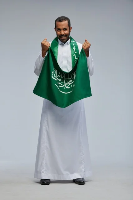 رجل سعودي يحمل العلم الوطني في وضعية احتفالية