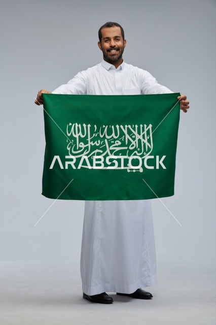 رجل سعودي يحمل العلم الوطني السعودي على خلفية رمادية