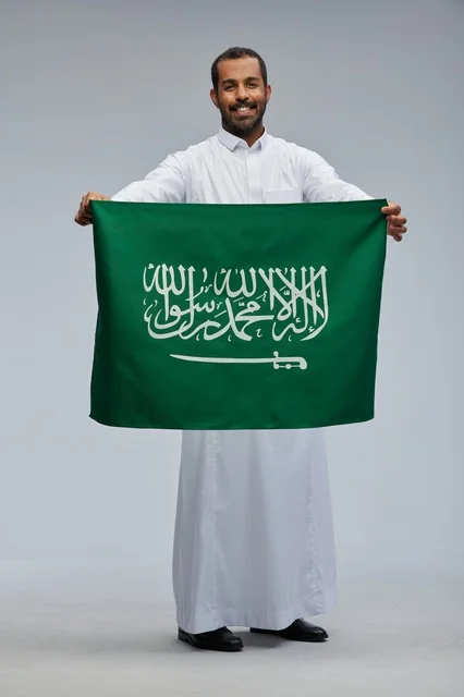 رجل سعودي يحمل العلم الوطني السعودي على خلفية رمادية