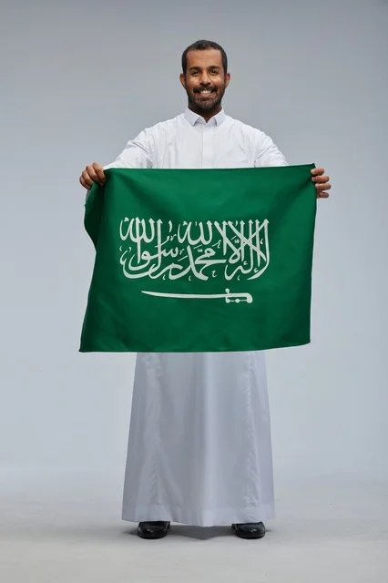 رجل سعودي يحمل العلم الوطني السعودي بالثوب التقليدي