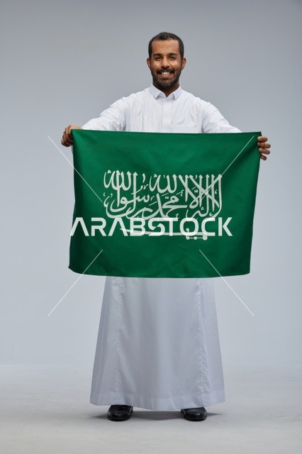 رجل سعودي يحمل العلم الوطني بالثوب التقليدي