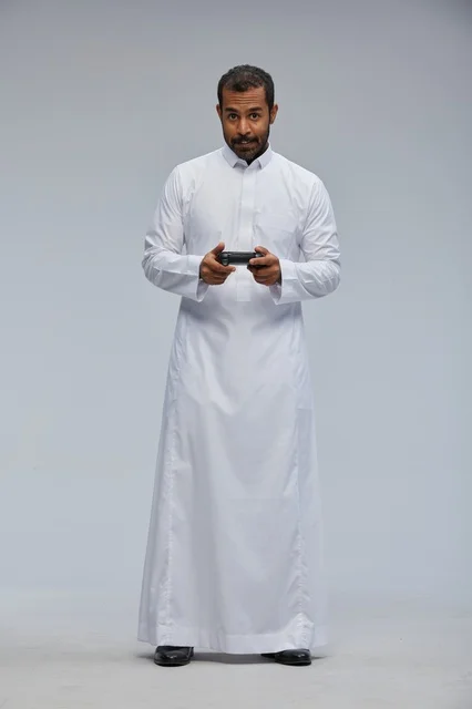 رجل سعودي بالثوب التقليدي يمسك بجهاز تحكم الألعاب