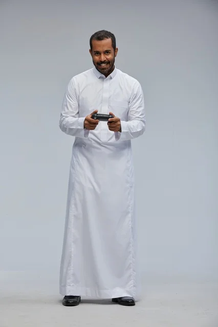 رجل سعودي بالثوب التقليدي يحمل جهاز تحكم ألعاب