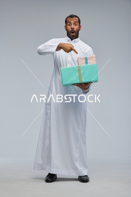 رجل سعودي بالثوب التقليدي يحمل صناديق هدايا مندهش