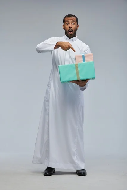 رجل سعودي بالثوب التقليدي يحمل صناديق هدايا مندهش