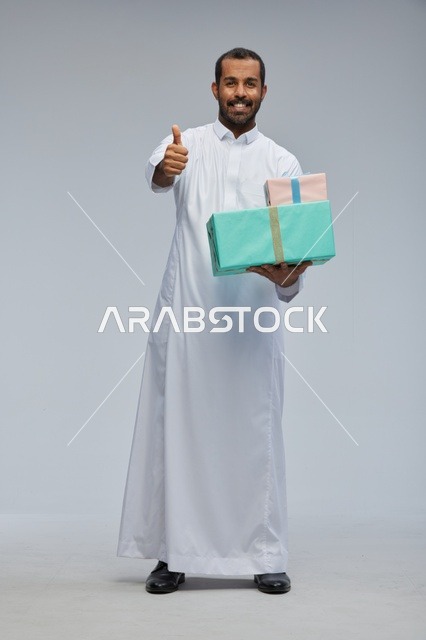 رجل سعودي يحمل صناديق هدايا مع إشارة الإبهام