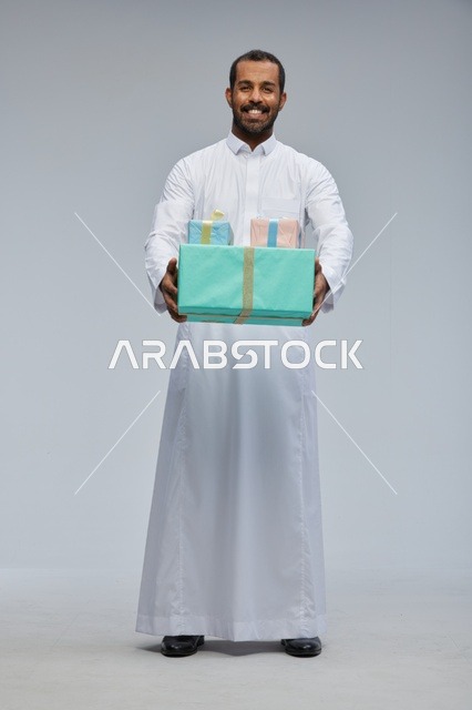 رجل سعودي بالزي التقليدي يحمل صناديق هدايا ملونة