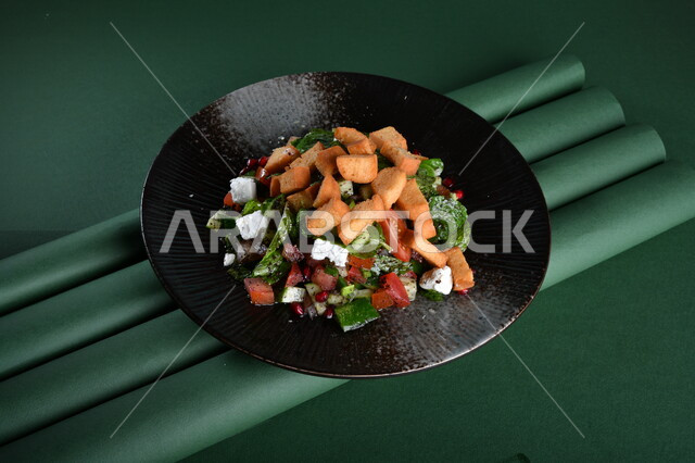 طبق سلطة الخضار اللذيذ ، مزين بقطع الخبز المقلية المقرمشة والجبنة البيضاء مصورة على خلفية خضراء ، مقبلات باردة ،  اطباق عربية ، ماكولات شرقية ، مقبلات رمضانية ، كروما ، طبق صحي ومفيد