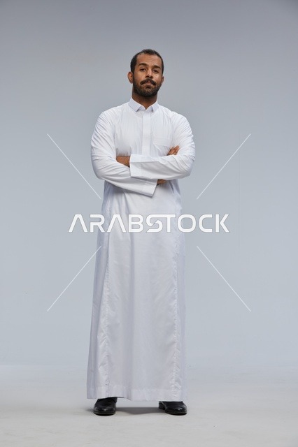 رجل سعودي بالثوب الأبيض يقف بوضعية مكتوفة الذراعين
