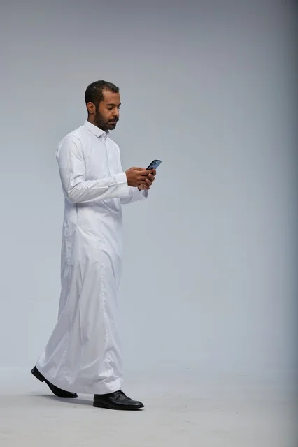 رجل سعودي بالثوب الأبيض يستخدم الجوال أثناء المشي