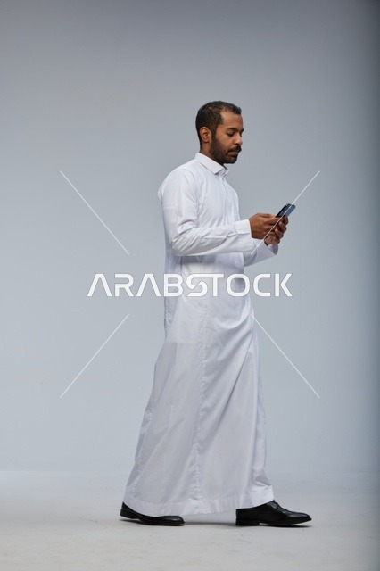 Saudi Man in White Thobe Using Smartphone on Grey Background