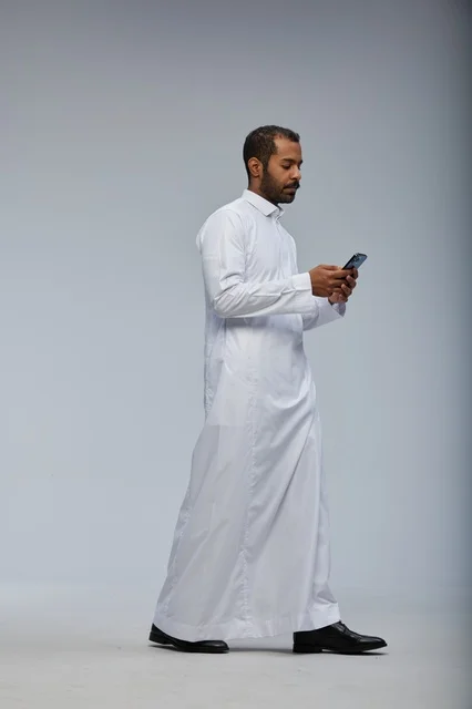 Saudi Man in White Thobe Using Smartphone on Grey Background