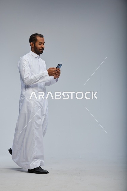 رجل سعودي بالثوب الأبيض يستخدم الهاتف الذكي في الاستوديو