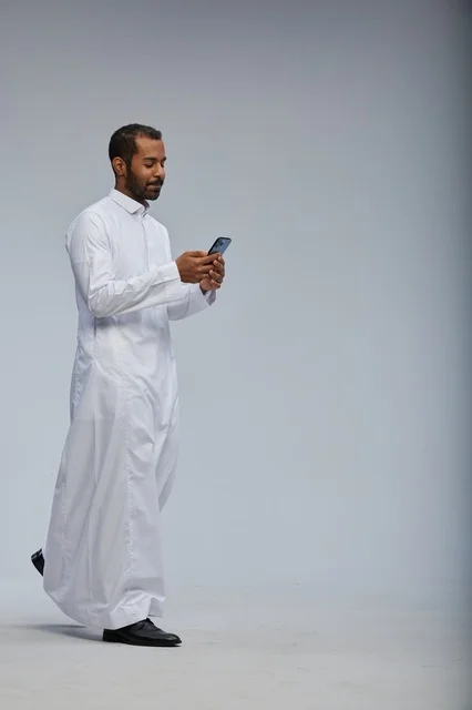 رجل سعودي بالثوب الأبيض يستخدم الهاتف الذكي في الاستوديو