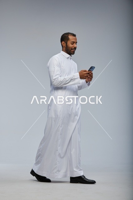 رجل سعودي بالثوب الأبيض يستخدم هاتف ذكي في استوديو