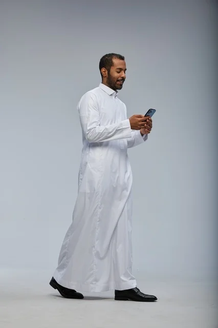 رجل سعودي بالثوب الأبيض يستخدم هاتف ذكي في استوديو