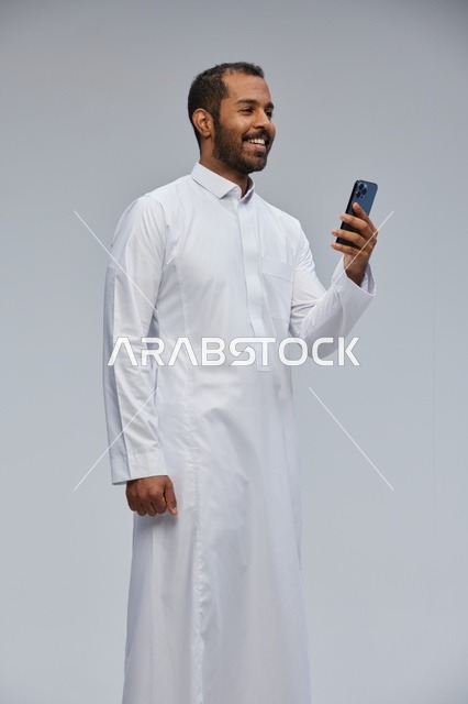 Saudi Man in White Thobe Using Smartphone