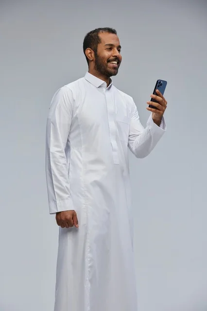 Saudi Man in White Thobe Using Smartphone