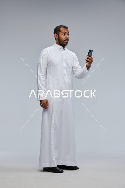 Surprised Saudi Man in White Thobe Using Smartphone