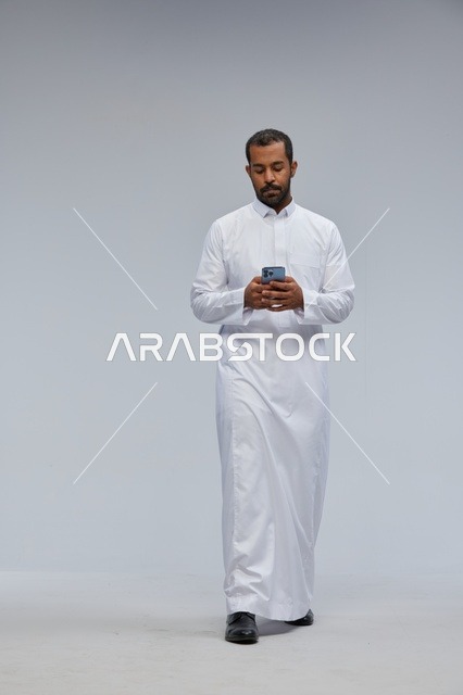 رجل سعودي بالثوب الأبيض يستخدم الجوال في الاستوديو