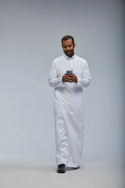 رجل سعودي بالثوب الأبيض يستخدم هاتف ذكي في الاستوديو