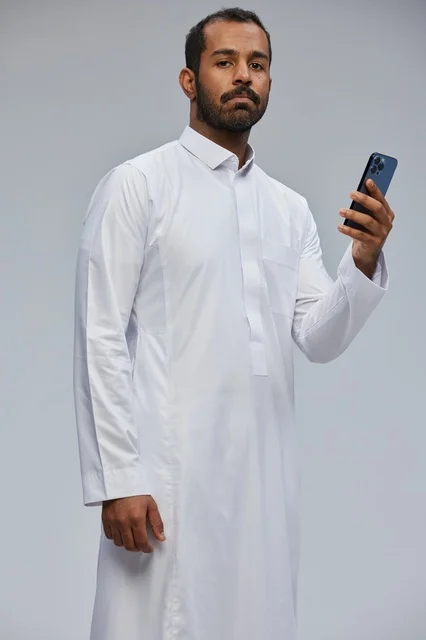 رجل سعودي بالثوب الأبيض يستخدم الهاتف الذكي في الاستوديو