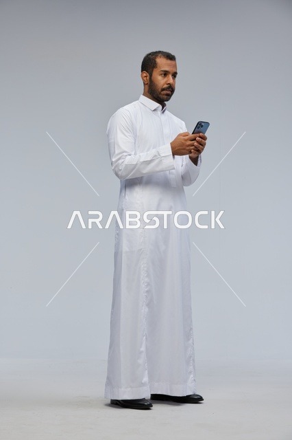 رجل سعودي بالثوب الأبيض يستخدم الهاتف الذكي في الاستوديو