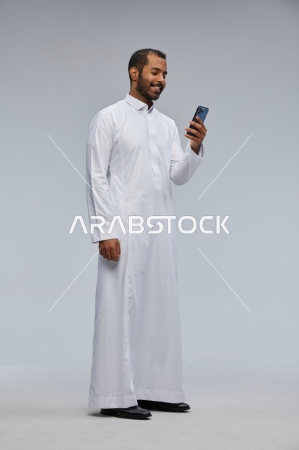 Saudi Man in White Thobe Using Smartphone