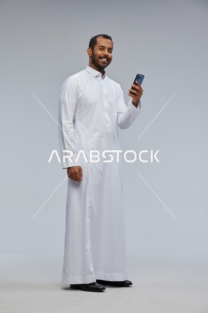 رجل سعودي بالثوب الأبيض يستخدم هاتفاً ذكياً
