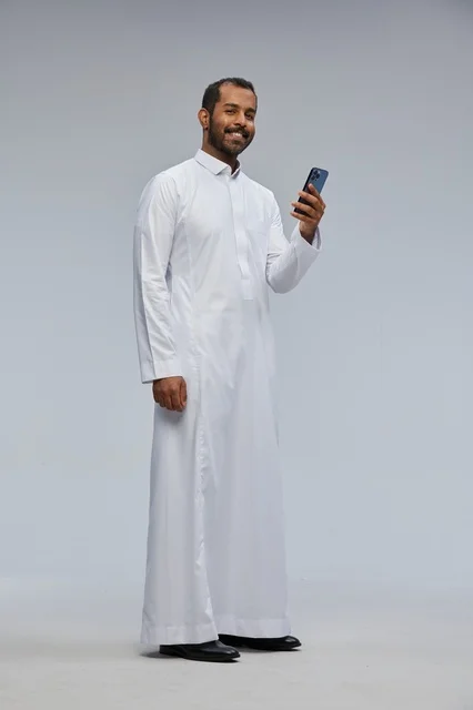 رجل سعودي بالثوب الأبيض يستخدم هاتفاً ذكياً