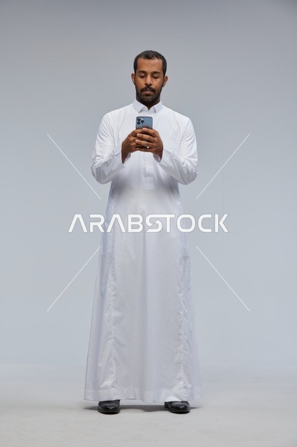 Saudi Man in White Thobe Using Smartphone