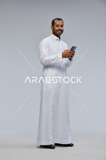 رجل سعودي بالثوب الأبيض يستخدم الجوال في استوديو