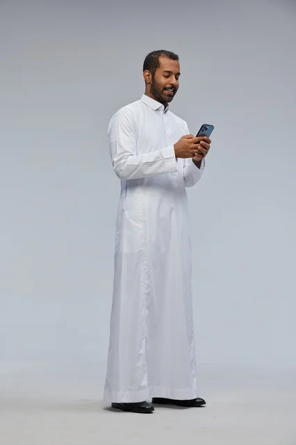 Saudi Man in White Thobe Using Smartphone on Gray Background