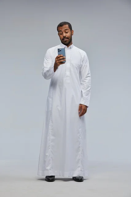 رجل سعودي بالثوب الأبيض يستخدم هاتف ذكي في الاستوديو