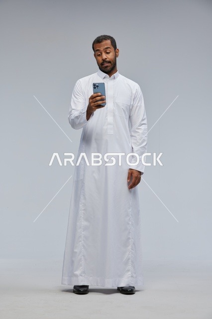 رجل سعودي يرتدي الثوب التقليدي يستخدم الهاتف الذكي