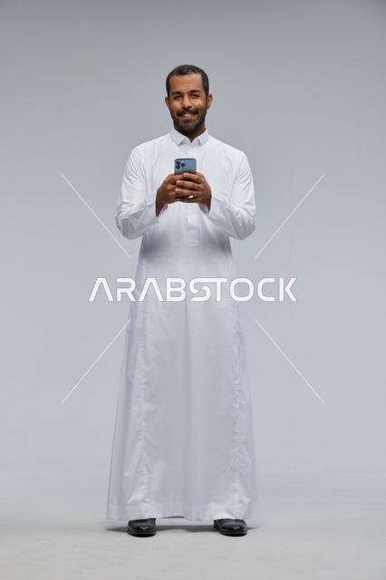 Saudi Man in White Thobe Using Smartphone Studio Portrait