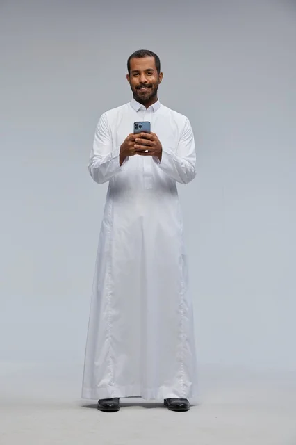 رجل سعودي بالثوب الأبيض يستخدم الهاتف الذكي في الاستوديو