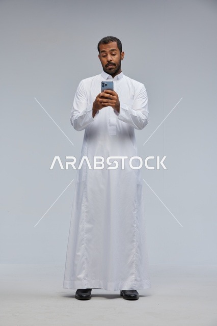 رجل سعودي بالثوب الأبيض يستخدم الهاتف الذكي في الاستوديو
