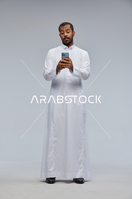 Saudi Man in White Thobe Using Smartphone Studio Shot