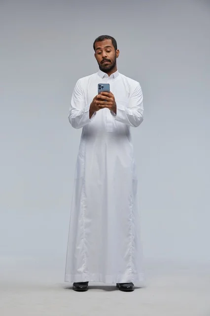 رجل سعودي بالثوب الأبيض يستخدم الهاتف الذكي في الاستوديو