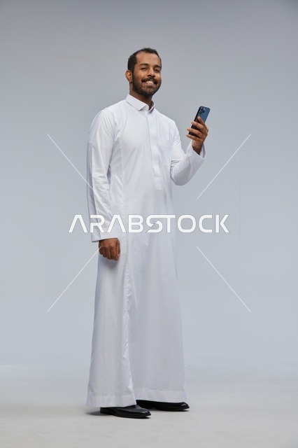 رجل سعودي بالثوب الأبيض يستخدم الهاتف الذكي في الاستوديو