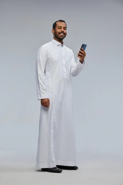 رجل سعودي بالثوب الأبيض يستخدم الهاتف الذكي في الاستوديو