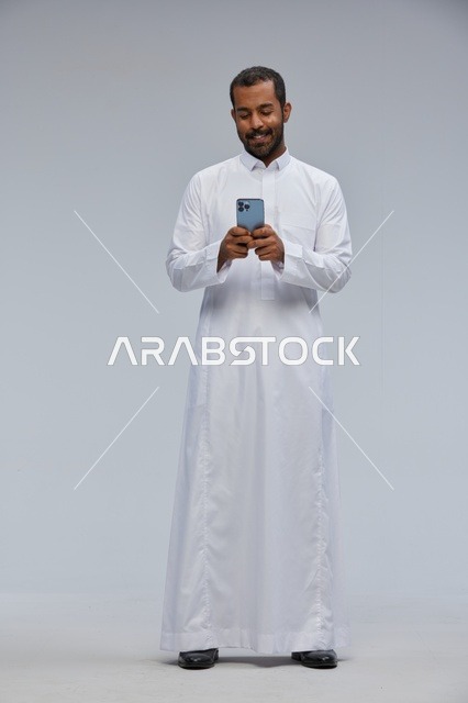 Saudi Man in White Thobe Using Smartphone