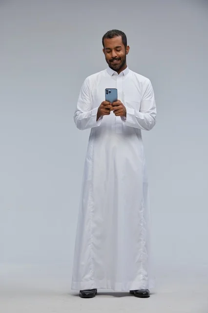 رجل سعودي بالثوب الأبيض يستخدم هاتف ذكي