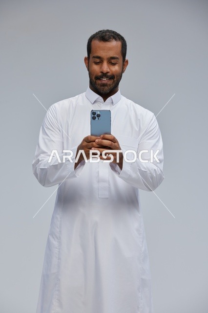 Saudi Man in White Thobe Using Smartphone