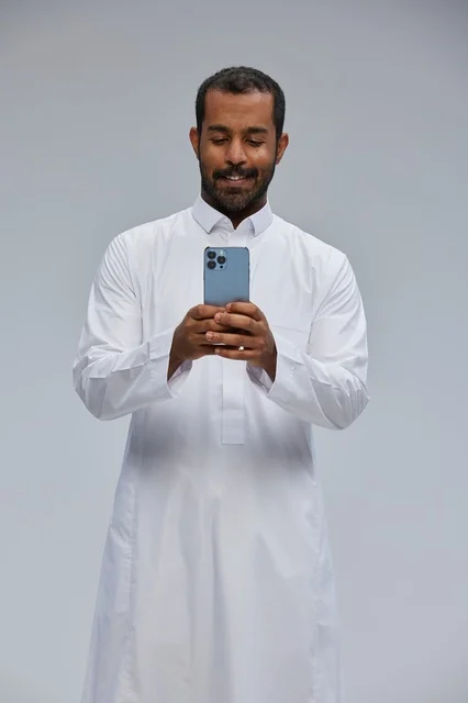 Saudi Man in White Thobe Using Smartphone