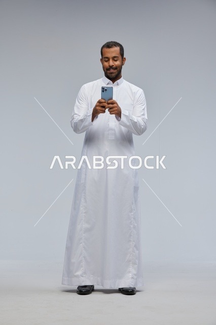 رجل سعودي بالثوب الأبيض يستخدم الهاتف الذكي في الاستوديو