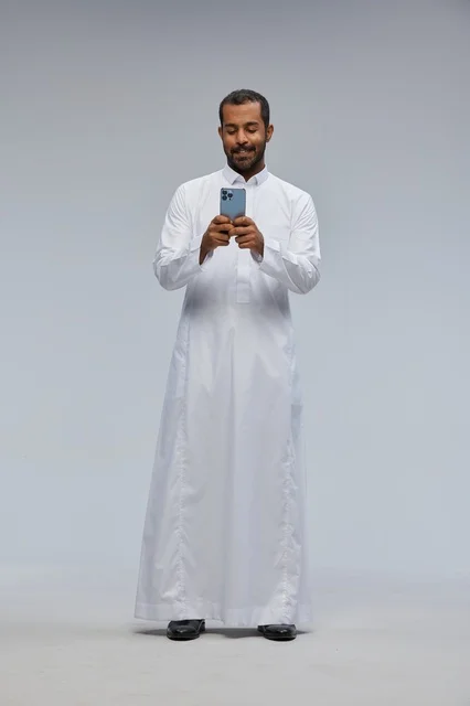 رجل سعودي بالثوب الأبيض يستخدم الهاتف الذكي في الاستوديو