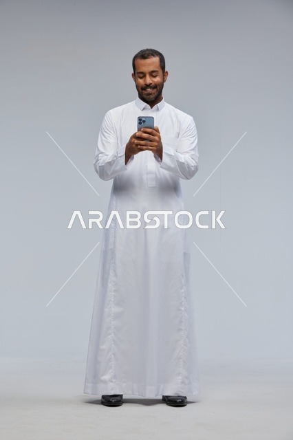 رجل سعودي بالثوب الأبيض يستخدم هاتف ذكي في الاستوديو