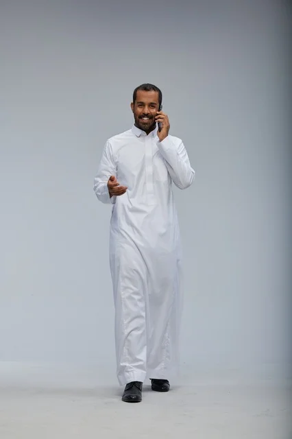 Saudi Man in White Thobe Talking on Smartphone